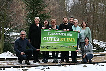 Der Landesvorstand - neun Frauen und Männer - halten das Poster hoch: "Zusammen für gutes Klima" - sie posieren im Winter neben dem Gebäude des Waldsolarheims in Eberswalde.