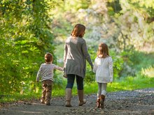 Eine Frau geht auf einem Waldweg mit ihrer ungefähr achtjährigen Tochter und dem vierjährigen Sohn. In einer entspannten, aber stillen Atmosphäre. Die drei Figuren sind von hinten fotografiert.